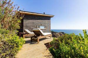 a wooden deck with two chairs and a tiny house at Horizonte Infinito in Tunquén