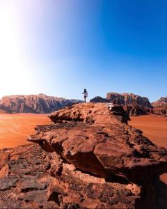 a person standing on top of a rock in the desert at Skylight Wadi Rum Camp in Disah