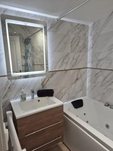 a bathroom with a sink and a tub and a mirror at Maison chaleureuse jacuzzi PS2-1, climatisation et parking payants in Bagneux