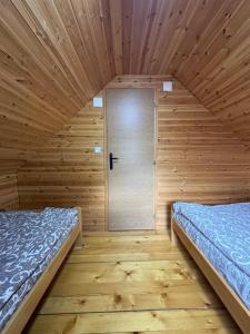 two beds in a wooden room with a door at Zaovinski Raj2 Tara in Konjska Reka