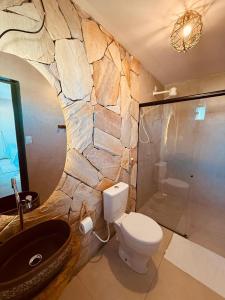 a bathroom with a toilet and a stone wall at Pousada Villa Velejo in Grossos