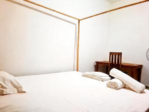 a white bed with two rolled towels and a chair at Bee Rooms Nosy be in Ambatoloaka