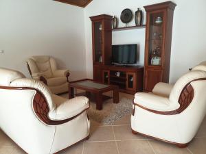 a living room with two white chairs and a tv at Farol Golfe in Ponta do Pargo