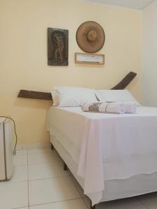 a bed with white sheets and a hat on the wall at Pousada Santa Adélia - Boipeba BA in Ilha de Boipeba