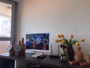 a desk with a computer monitor and a vase with flowers at Barrah flat in Barra de São Miguel