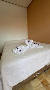 a bed with white towels and purple flowers on it at Cantinho dos Pássaros Centro Penedo RJ in Penedo
