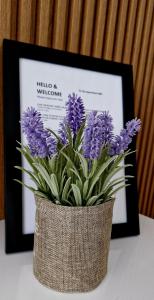 a vase with purple flowers in front of a framed picture at Apartman A&V in Banja Luka