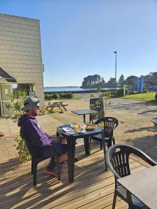 a man sitting at a table on a deck at Camping de l'Espérance - Camping Côte de granit rose - Trébeurden - Ile grande - GR34 in Trébeurden