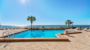 a swimming pool with palm trees and the beach at Gull Watch by AvantStay in Panama City Beach