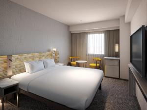 a hotel room with a large white bed and a television at Mitsui Garden Hotel Okayama in Okayama