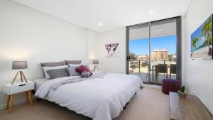 a white bedroom with a bed and a large window at Oceans Edge #7 Accom Holidays in Terrigal