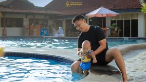 a man holding a baby in front of a swimming pool at Royal Brongto Hotel in Yogyakarta +46 photos