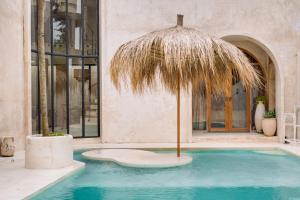 a pool with a straw umbrella in front of a building at South Villa Ungasan in Ungasan