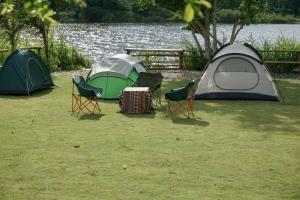 three tents and chairs on the grass near a body of water at The Forester Chalet in Buôn Pưk Prong