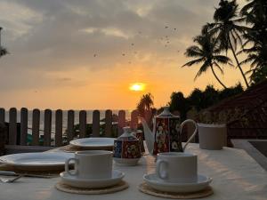 a table with cups and plates on it with the sunset at Villa Nature Glee in Dodanduwa