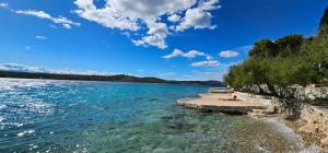 a group of people sitting on the shore of a body of water at Beach front with Swimming pool, Illyria Resort Apt 101 in Milna