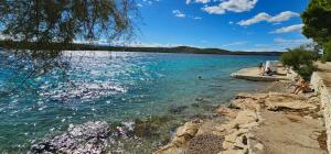 a body of water with people sitting on the shore at Beach front with Swimming pool, Illyria Resort Apt 101 in Milna +5 photos
