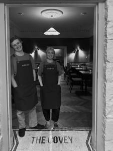 two people wearing aprons are standing in a doorway at Lyzzick in Keswick