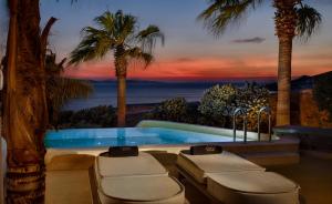 a swimming pool with palm trees and a sunset at Anax Resort and Spa in Agios Ioannis Mykonos