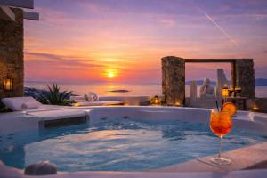 a jacuzzi tub with a drink in it with a sunset at Tharroe of Mykonos Boutique Hotel in Mikonos