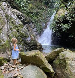 a little girl standing on rocks in front of a waterfall at Reserva Wanaka, San Carlos in Cocorná