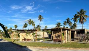 a building with chairs and palm trees in the background at Bangalôs Riviera do Patacho in Pôrto de Pedras