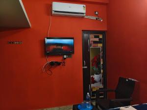 a room with an orange wall with a flat screen tv at Ocean Wind Homestay in Pondicherry