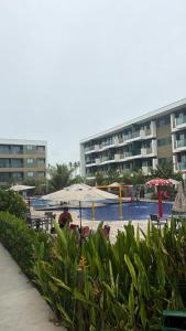a person sitting under an umbrella near a swimming pool at Mana Experience Muro Alto in Porto De Galinhas