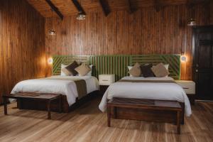 two beds in a room with wooden walls and wood floors at Lauraceas Lodge in San Gerardo de Dota