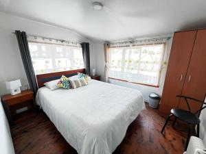 a bedroom with a large white bed and two windows at Fungi Hostal in Coihaique