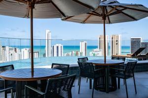 two tables with chairs and umbrellas on a balcony at Flat Luxo em Boa Viagem - 5min do Aeroporto - perto da praia - Wi-Fi 500mb - check-in 24h in Recife