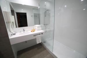 La salle de bains blanche est pourvue d'un lavabo et d'une douche. dans l'établissement Hotel Plaza - site du Futuroscope, à Chasseneuil-du-Poitou