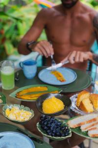 a shirtless man sitting at a table with plates of food at LAUS Bangalôs Experience - Piscina Privativa - Praia de Algodões - Península de Maraú - Bahia in Praia dos Algodões