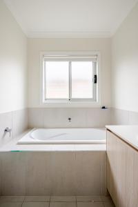 a white bathroom with a tub and a window at Neat and tidy house in Cranbourne +19 photos