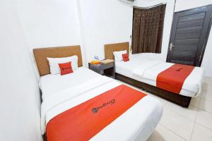 two beds in a hotel room with red and white at RedDoorz at Lumungga Residence Lampung in Lampung