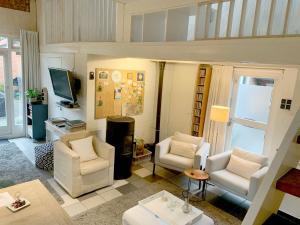 a living room with white chairs and a television at Gezellig Cottage Markdal met gratis fietsen in Breda