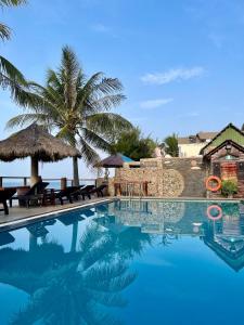 a swimming pool with a palm tree and a house at Viva Beach Resort Mui Ne in Mui Ne