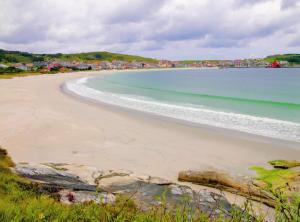 a beach with the ocean and buildings in the distance at Brisa do atlántico - Primera línea Laxe in Laxe +2 photos