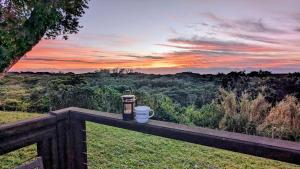 a view of a sunset from a fence with two coffee cups at Ocean View Nature Lodge in St Lucia