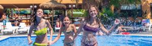 three women in bathing suits playing in a swimming pool at Camping Enmar - Mobil home 3 pièces 4 personnes climatisé + TV MAE-5300 in Pineda de Mar