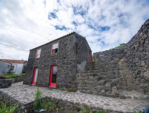 a stone building with red doors and a stone wall at Ribeirinha 94 in Ribeirinha