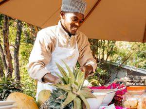 a man in an apron is cutting a pineapple at Mount Meru Game Lodge in Arusha