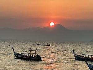 two boats in the water with the sunset in the background at Phayamhostel in Ko Phayam
