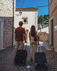 a man and woman walking down a street with luggage at Albergo Parco Gran Sasso in Castel del Monte