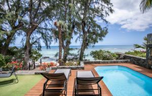 a swimming pool with chairs and a table and the ocean at Beach, Blue Sea, Sunset and Private Pool in Rivière Noire