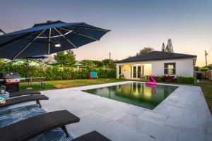 a swimming pool with an umbrella next to a house at Delray Oasis - Private Pool - Fenced Yard - Parking - Laundry - Full Kitchen - Convenient Location in Delray Beach