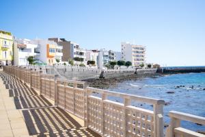 a fence next to a body of water with buildings at Apartamento en primera línea de la playa in Arinaga