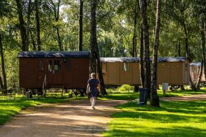 a woman walking down a dirt road in front of a cabin at Camping Papillon Kinrooi - Pipowagen 2p in Kinrooi