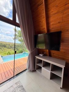 a living room with a tv and a large window at Vale dos Ventos - Chalés e Hospedagem in Jaboticatubas