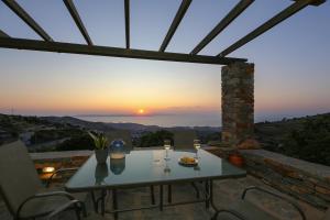 a table and chairs on a patio with a sunset at Cycladic Villa with sea view! in Ioulis +38 photos